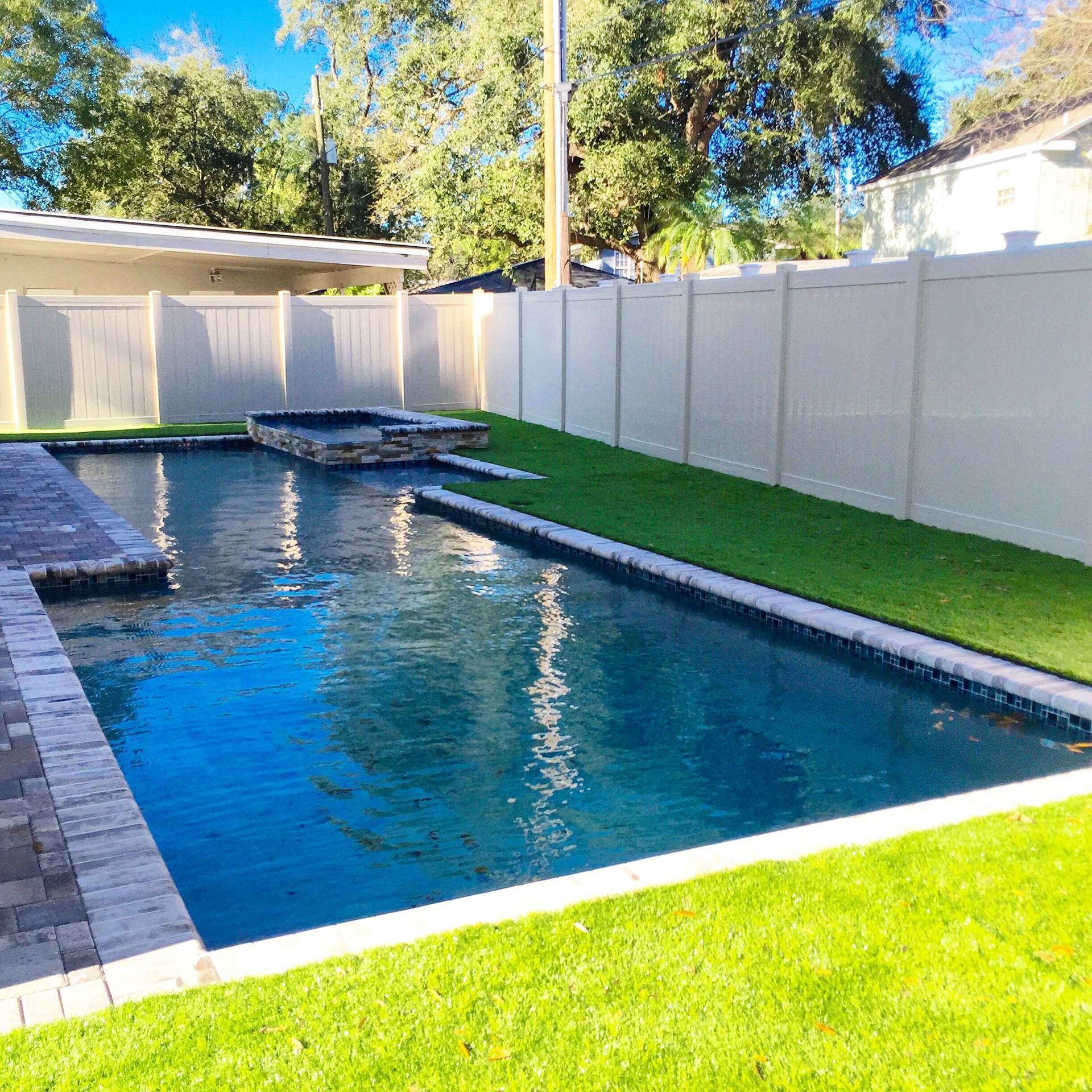 Backyard pool with white fence, green grass, and small hot tub.