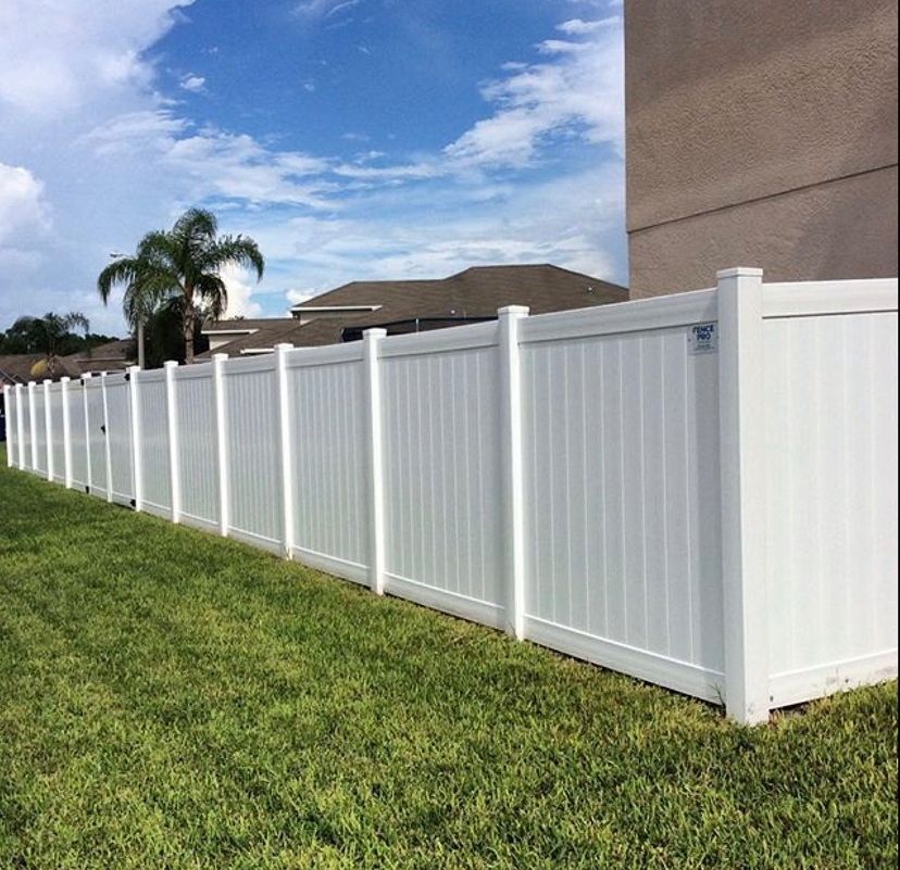 White vinyl fence in a grassy yard under a blue sky with clouds.