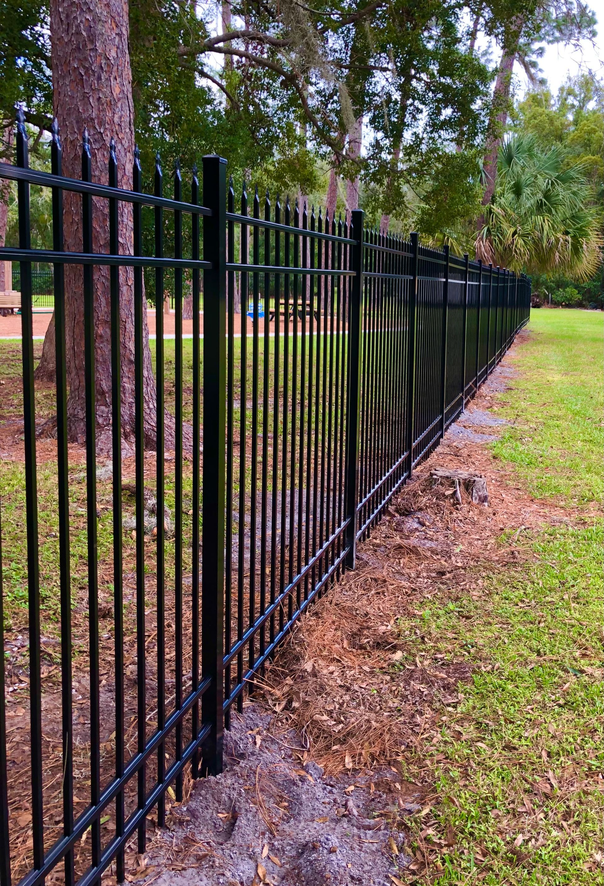 Black metal fence alongside grassy area and trees.