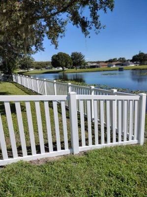 White picket fence bordering a lake under a clear, blue sky.