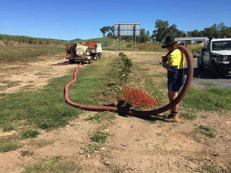 A Man Is Standing Next To A Large Hose In A Field — Mulch, Fencing And Landscaping Mackay, QLD