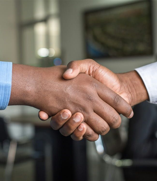 Dos personas vestidas de traje de negocios dándose la mano en un entorno de oficina.