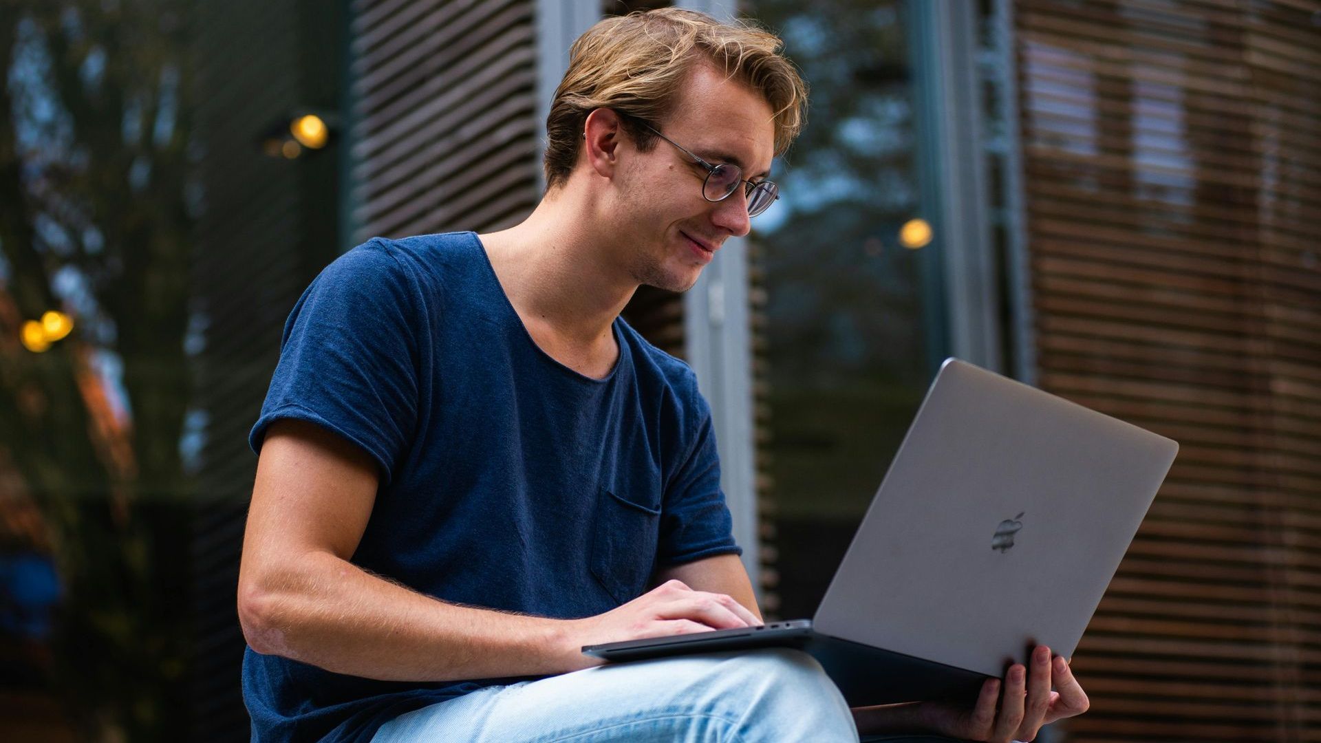 A man is sitting on the steps of a building using a laptop computer.