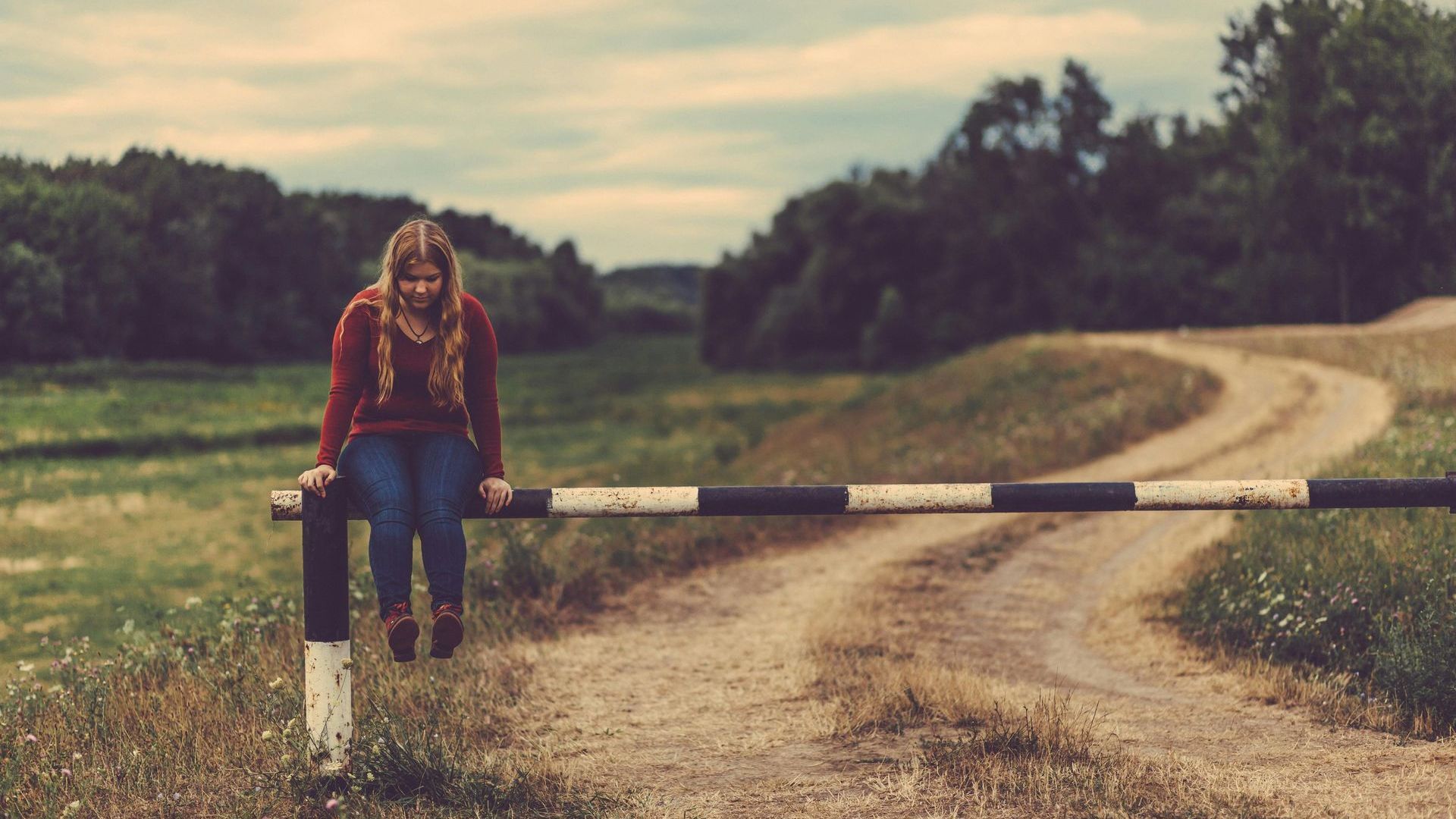 A woman is sitting on a railing on the side of a dirt road.