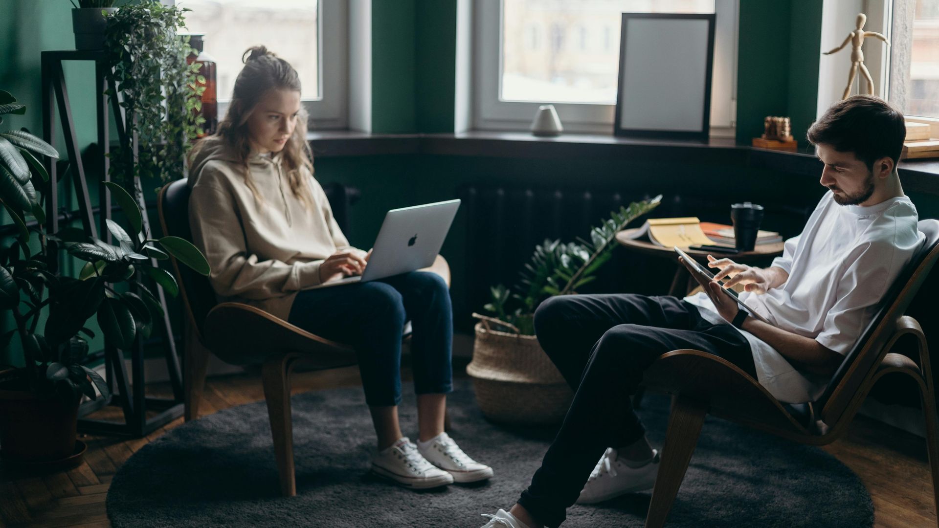 A man and a woman are sitting in chairs using laptops.