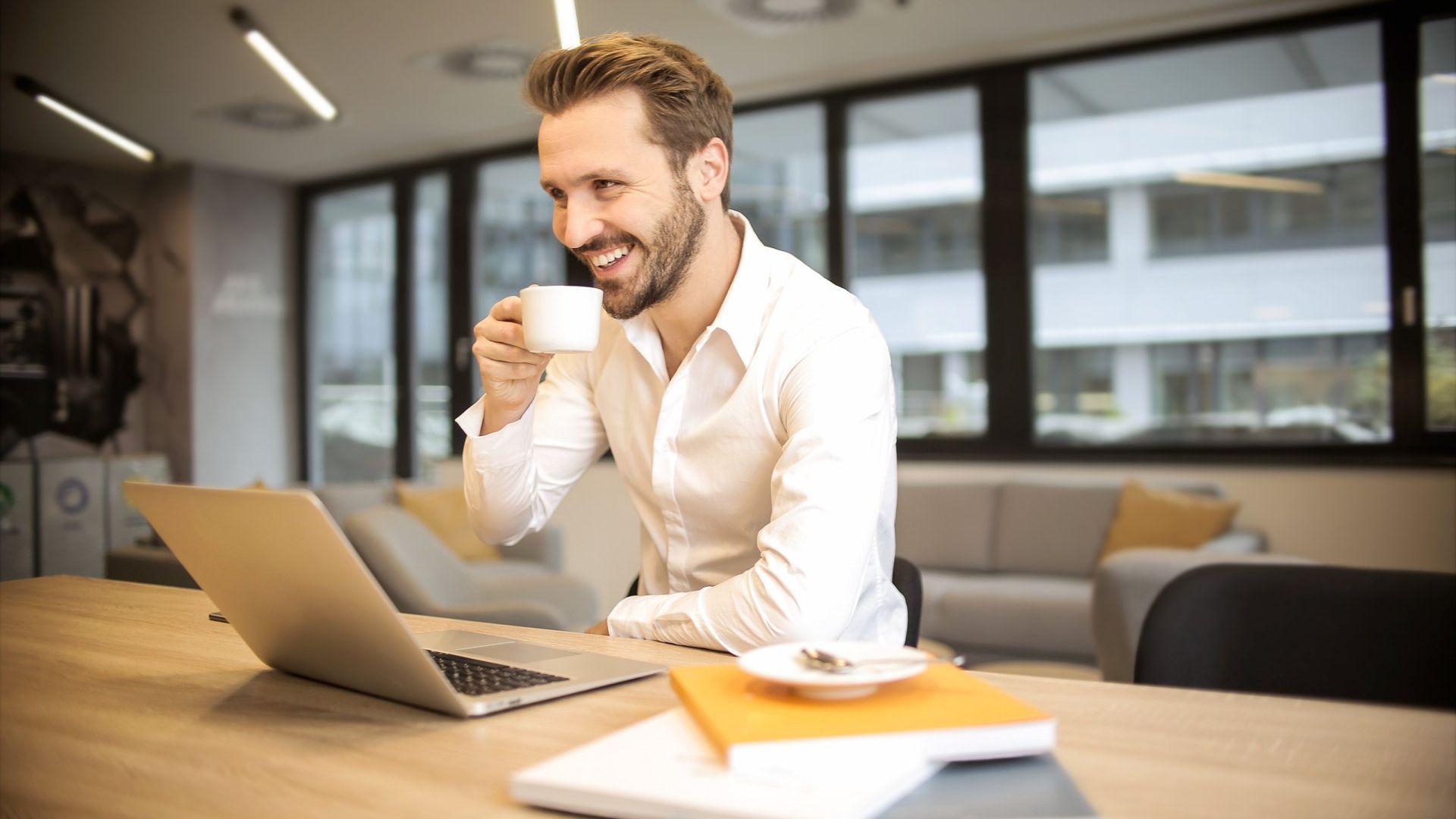 A man is drinking coffee while using a laptop computer.