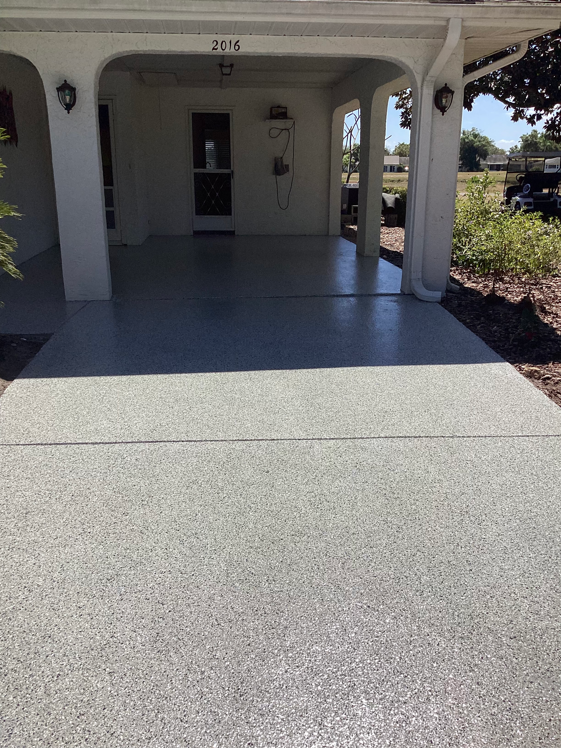 A gray concrete driveway with a white house in the background