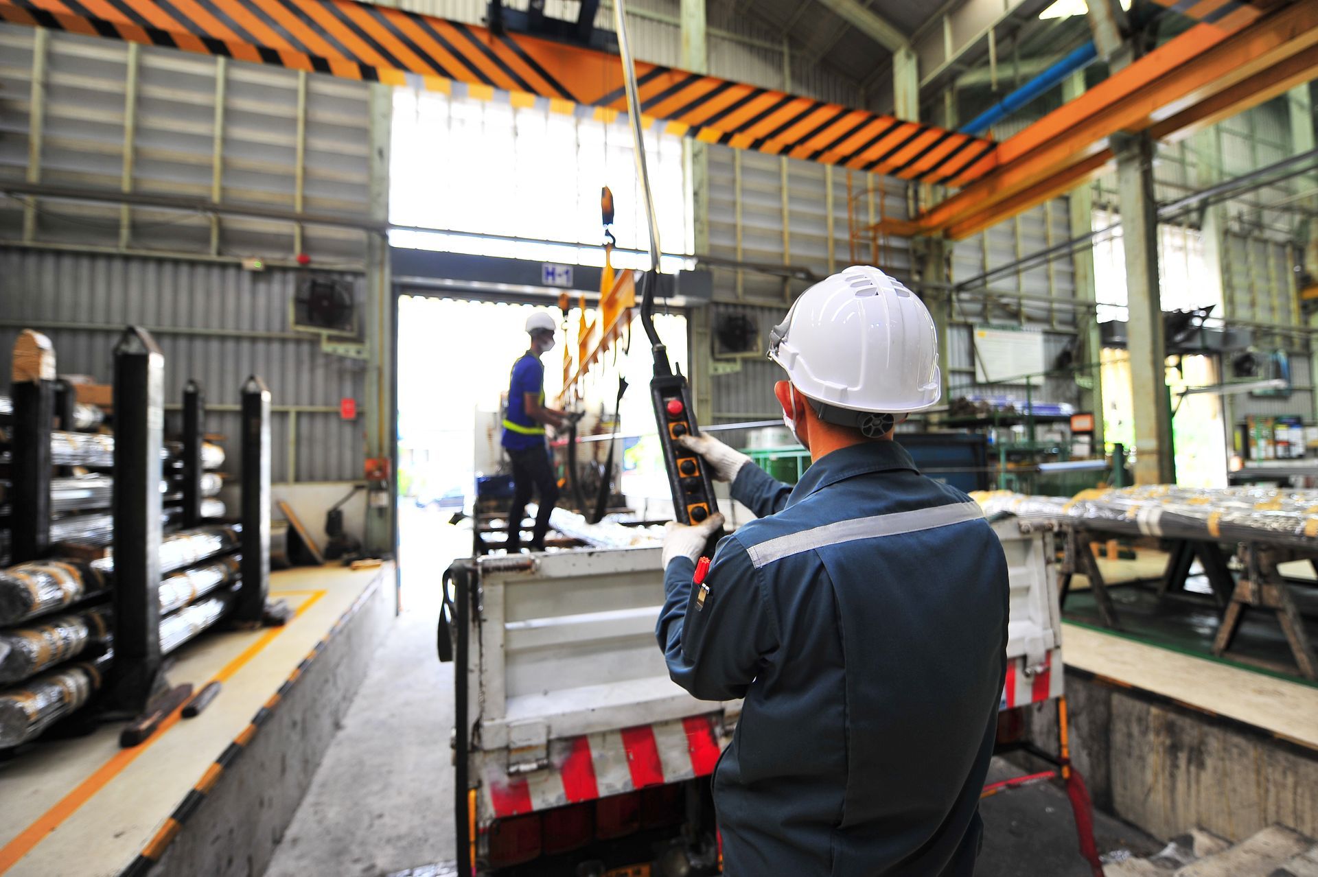 A man in a hard hat is standing next to a truck in a factory.