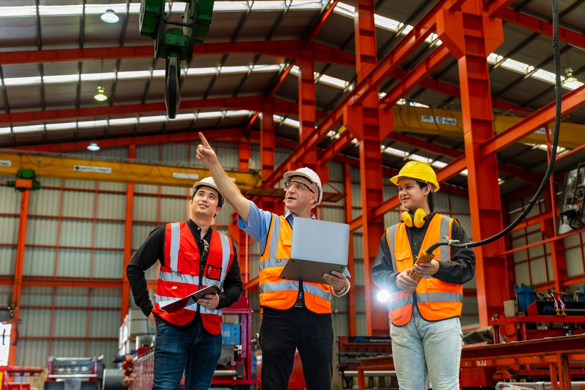 A group of construction workers are standing in a warehouse looking at a laptop.