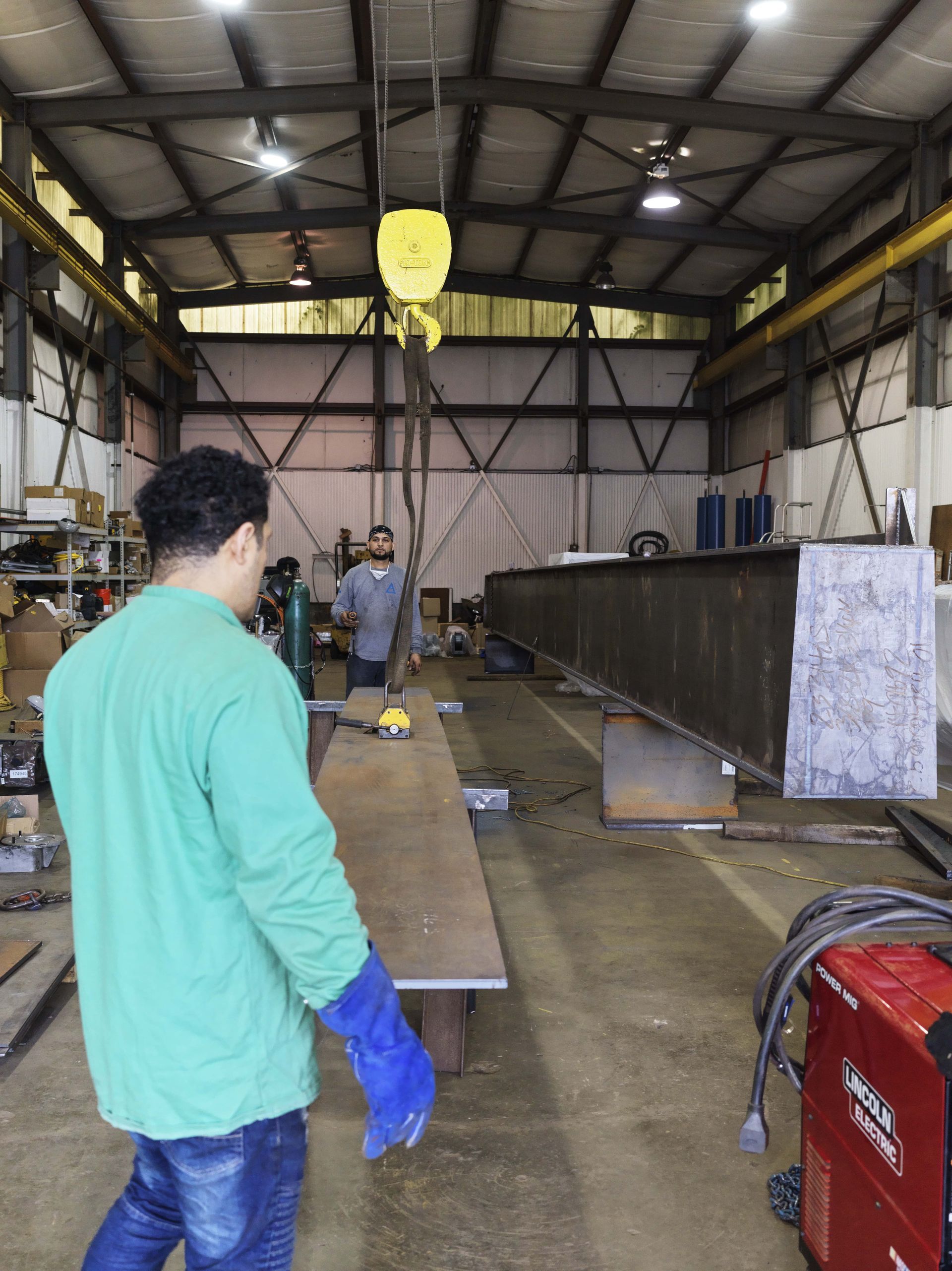 A man in a green shirt and blue gloves is standing in a factory.