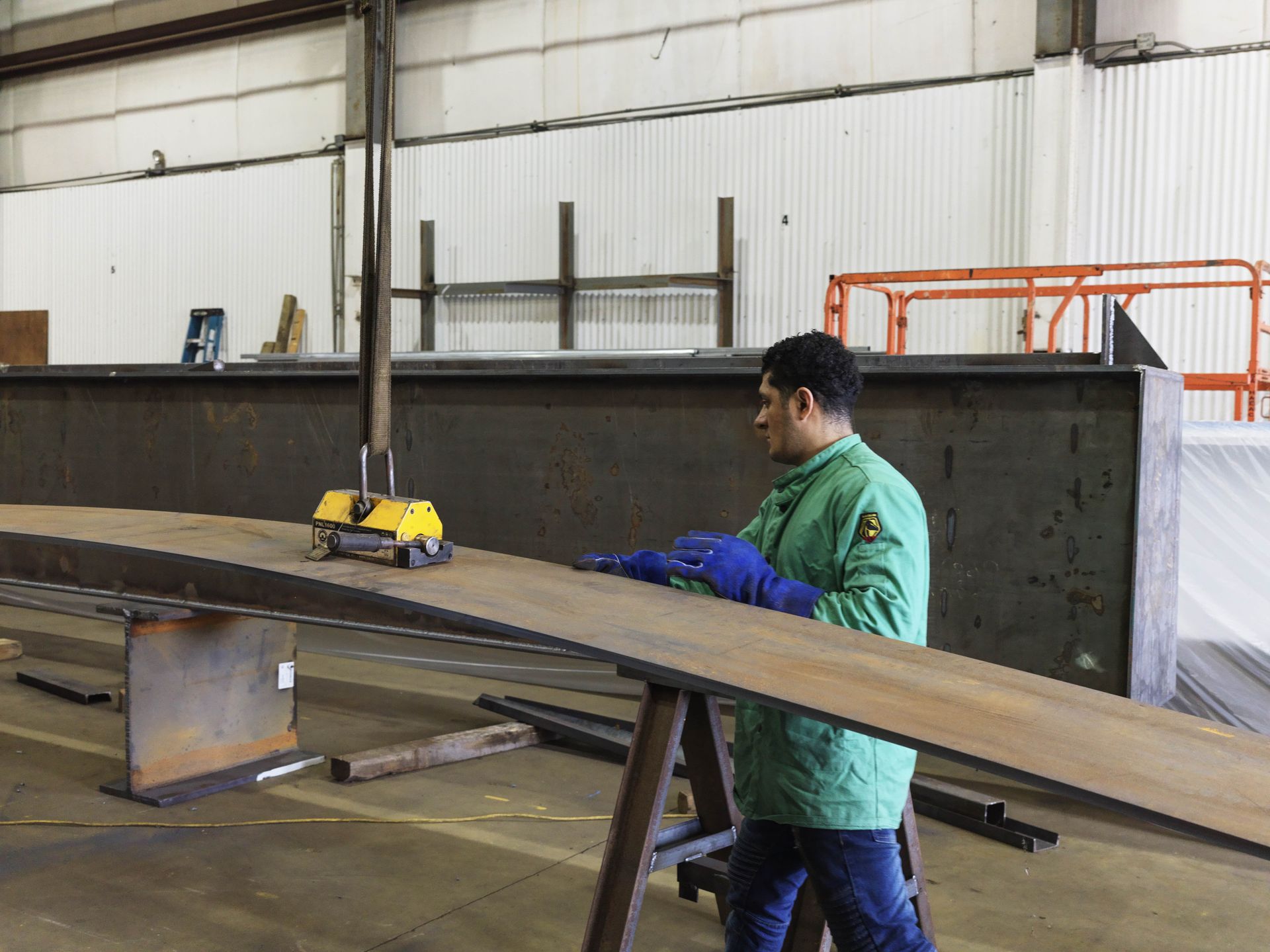 A man in a green jacket is working on a piece of metal in a factory.