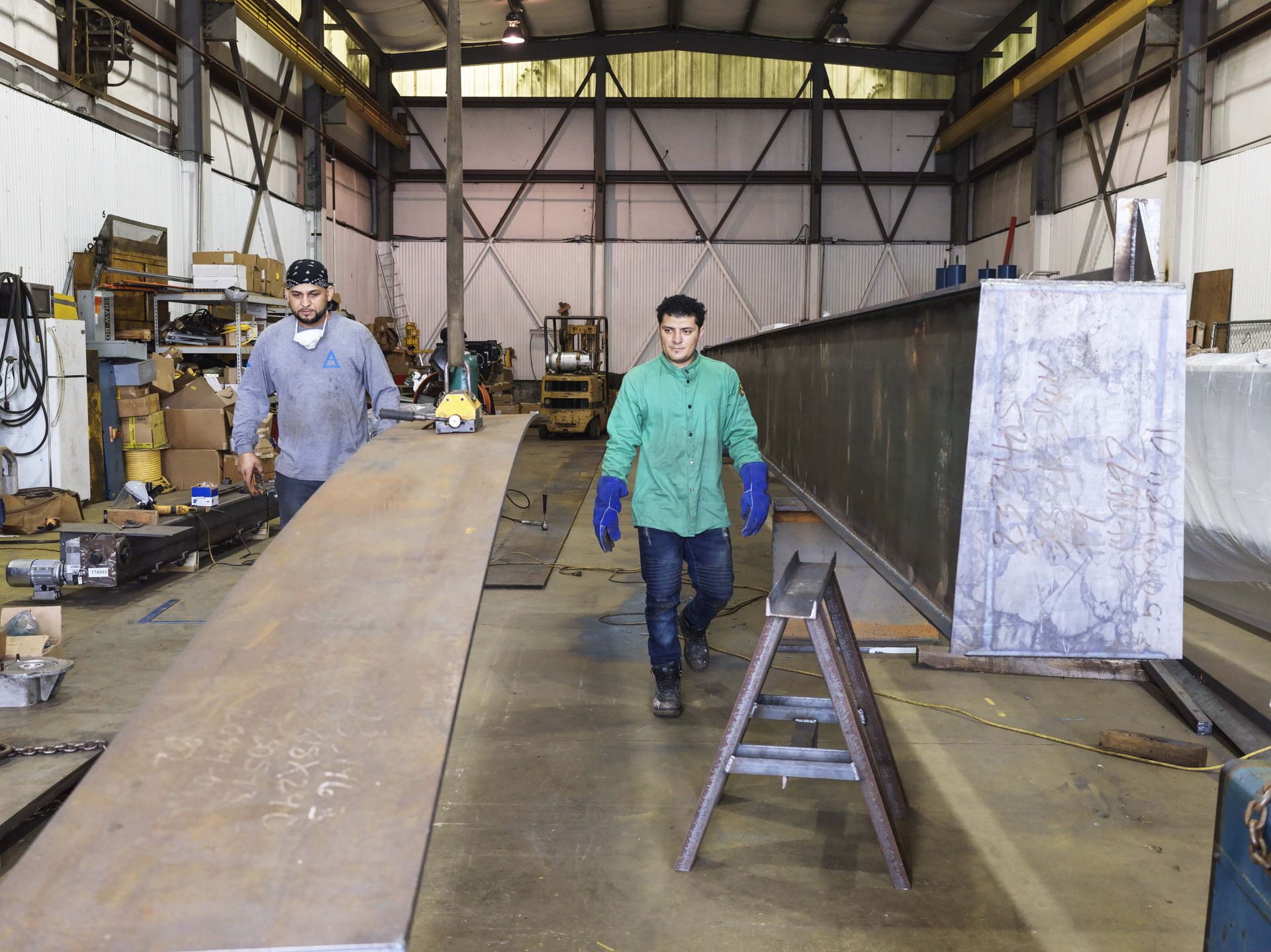 Two men are working on a large piece of metal in a factory