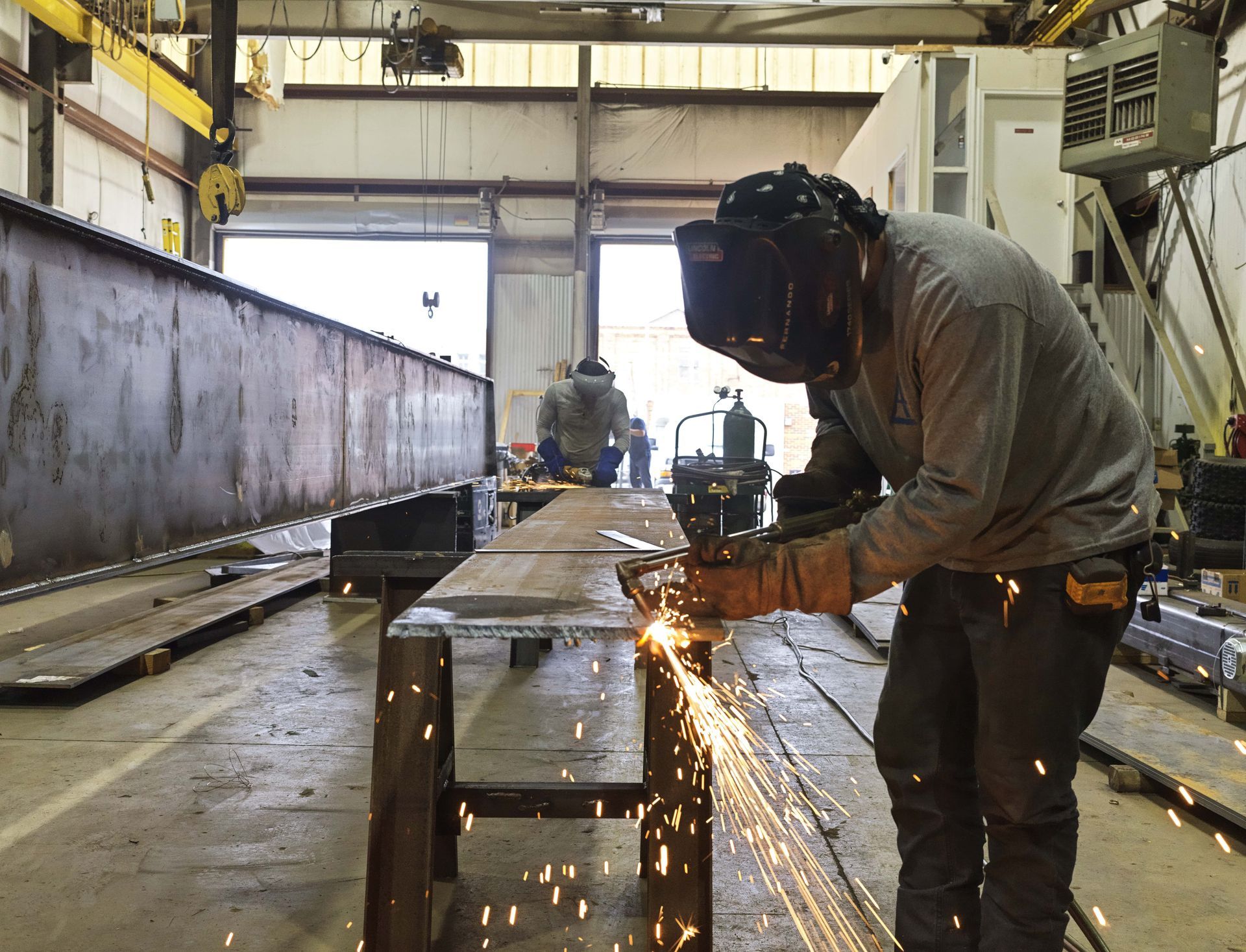 A man wearing a welding mask is cutting a piece of metal