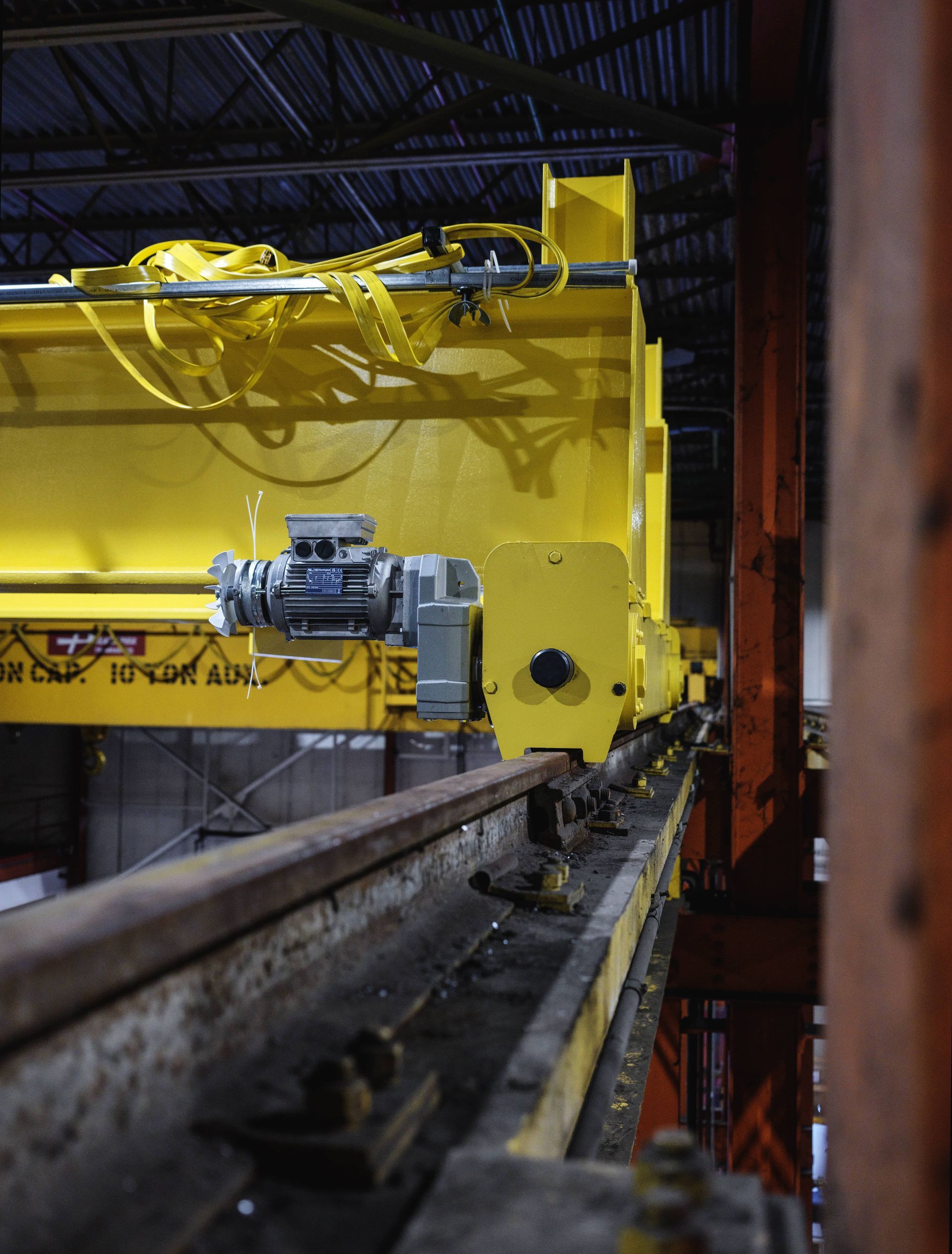 A yellow crane is sitting on a conveyor belt in a warehouse