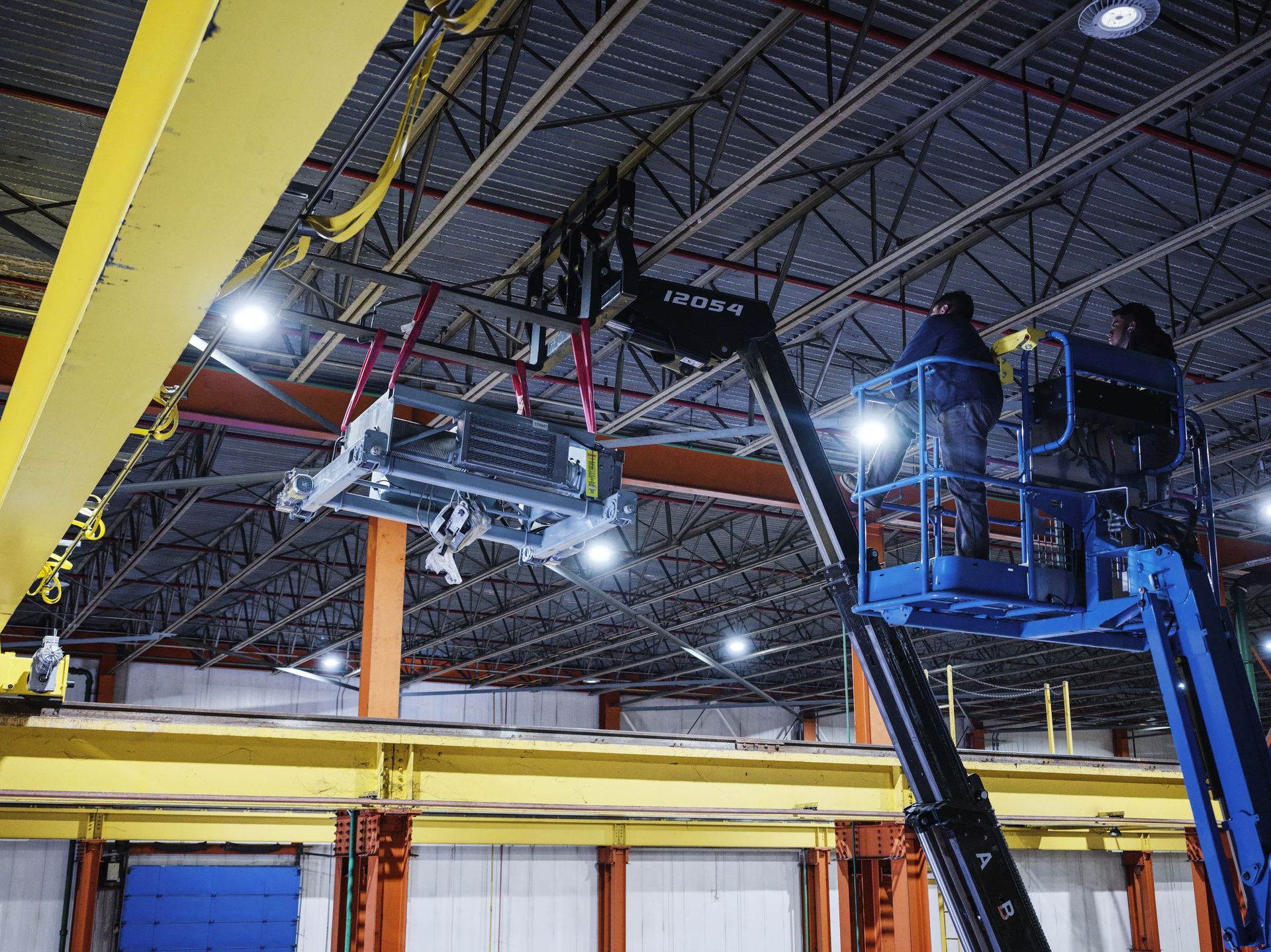 Two men are working on a crane in a factory.
