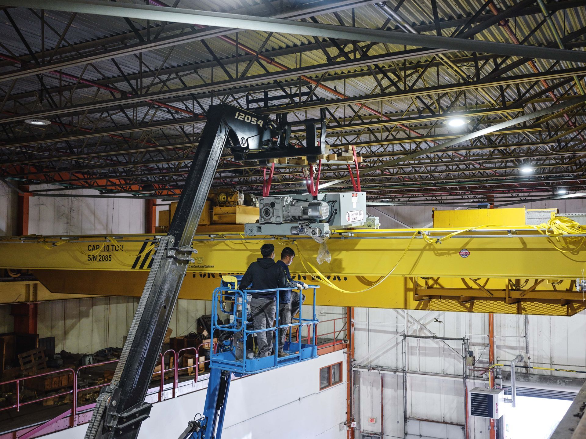 Two men are working on a crane in a warehouse.