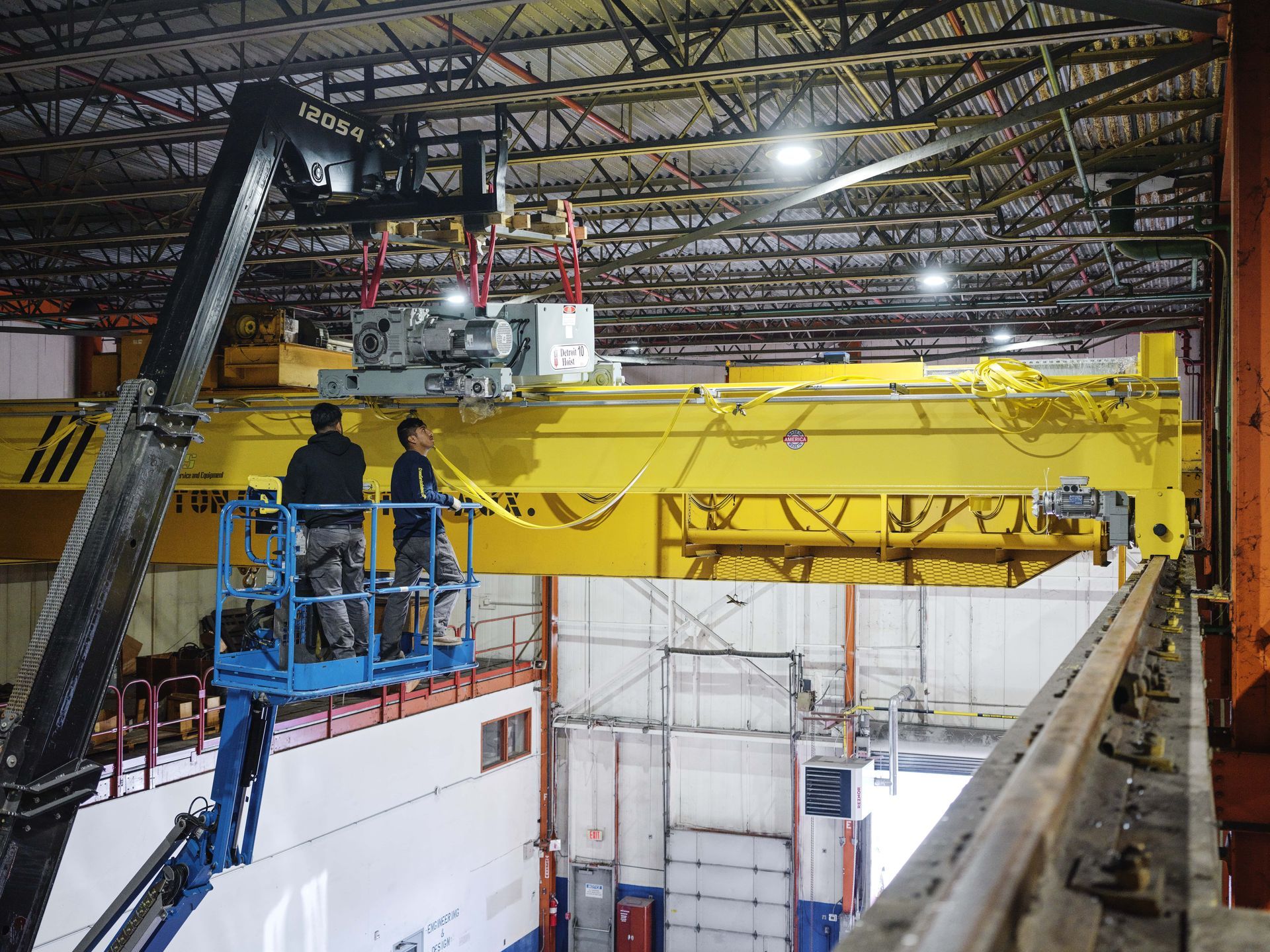 Two men are working on a crane in a warehouse.