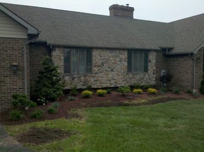 Single-story brick house with dark roof, front windows, and a landscaped flower bed.