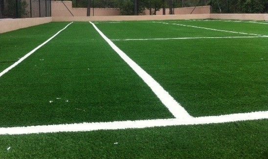 Un terrain en gazon artificiel vert avec des lignes blanches pour la pratique du sport, entouré d'une clôture.