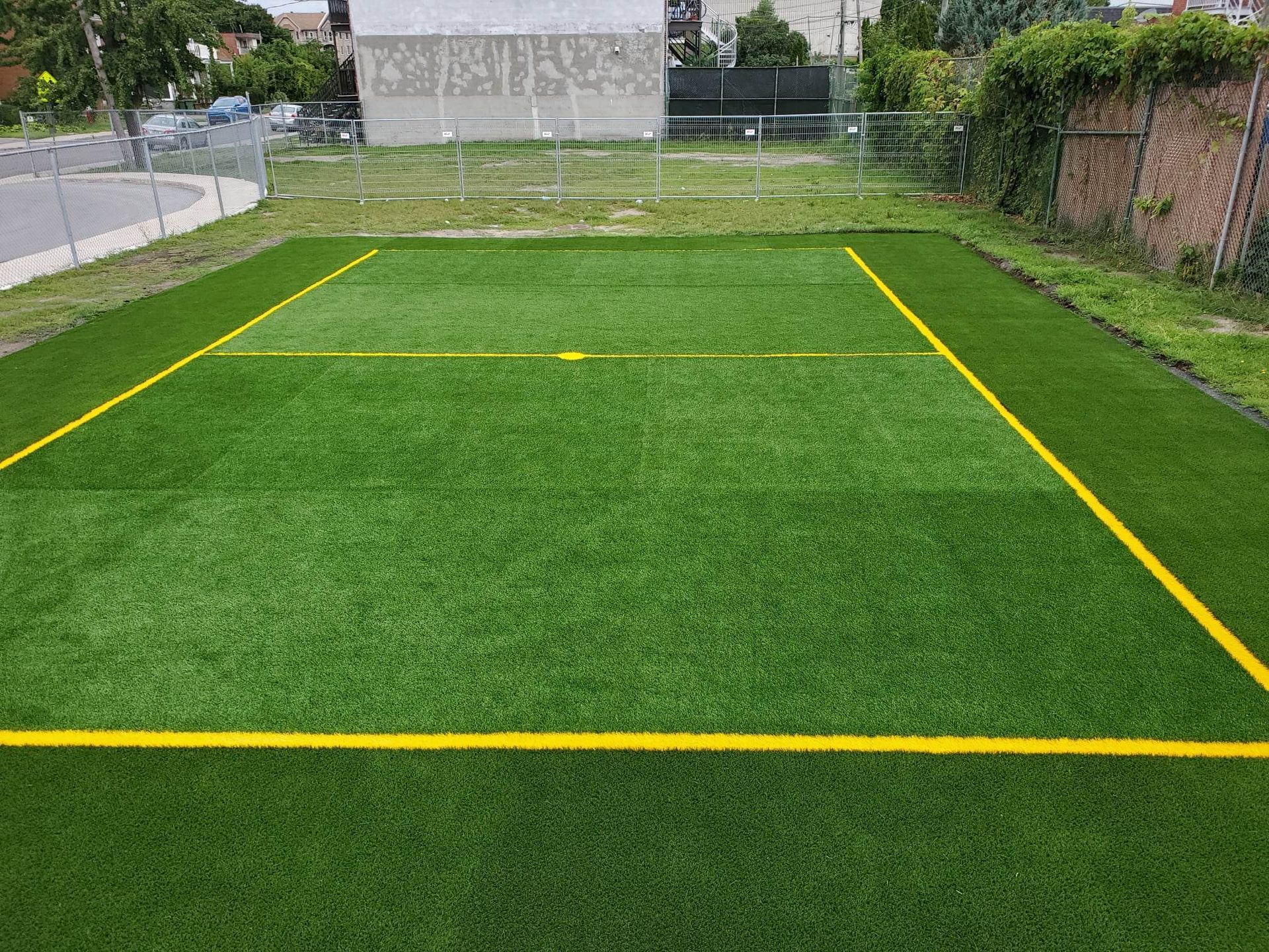 Un petit terrain en gazon vert délimité par des lignes jaunes. Un poteau de but est visible en arrière-plan.