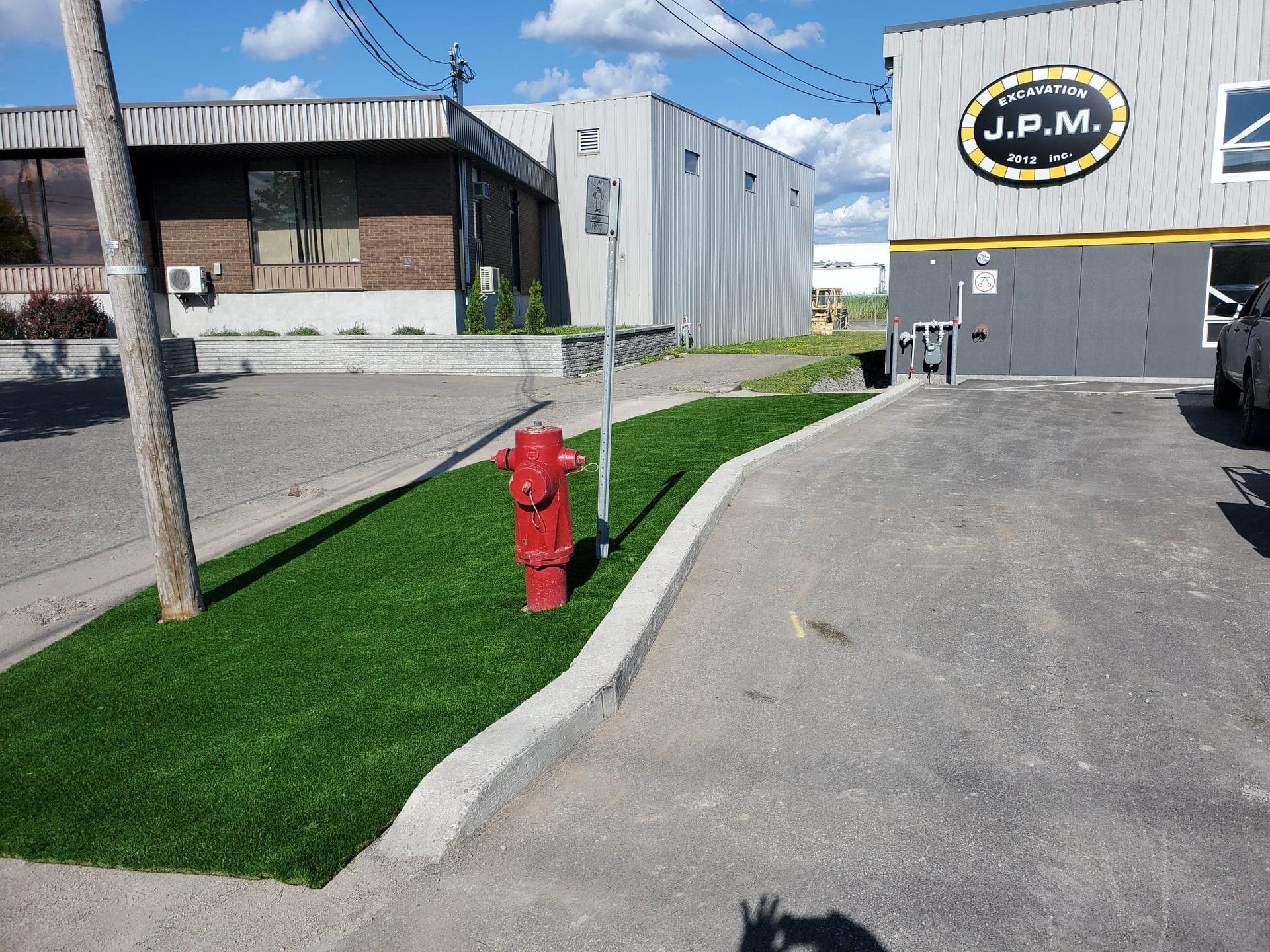 Une bouche d'incendie rouge se dresse dans une parcelle de gazon artificiel vert à côté d'un bâtiment et d'une allée par une journée ensoleillée.