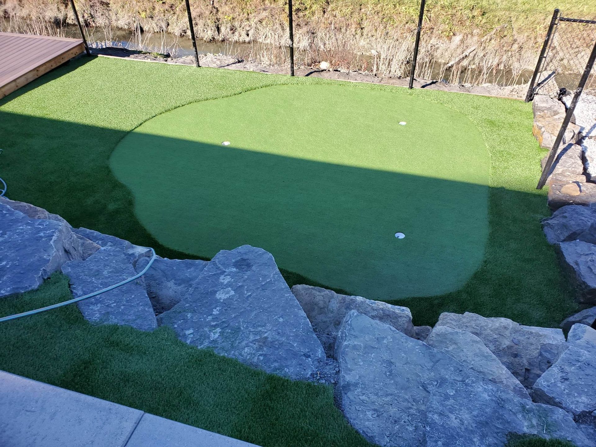 Un putting green dans l'arrière-cour avec deux balles de golf, entouré de rochers et d'une clôture noire.