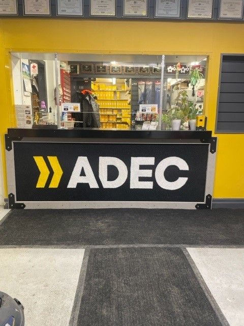 Un comptoir avec le logo « ADEC » en jaune et noir. Ce comptoir se trouve dans un magasin ou un bureau.