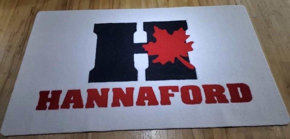 Un tapis blanc avec le logo Hannaford. Ce logo présente un « H » noir, une feuille d'érable rouge et le nom en lettres rouges.
