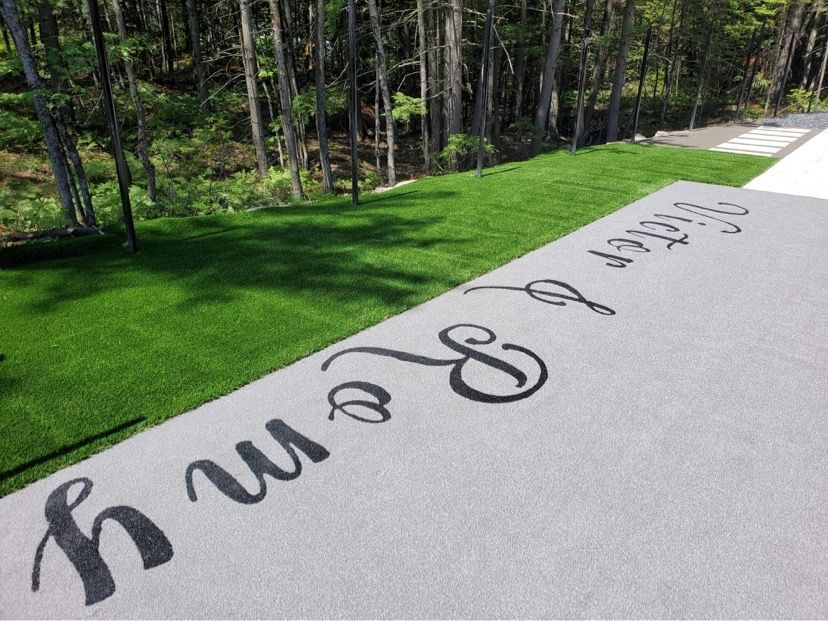 Patio gris avec lettrage noir « Riley & Remy » à côté d'une bande de gazon vert donnant sur une forêt.