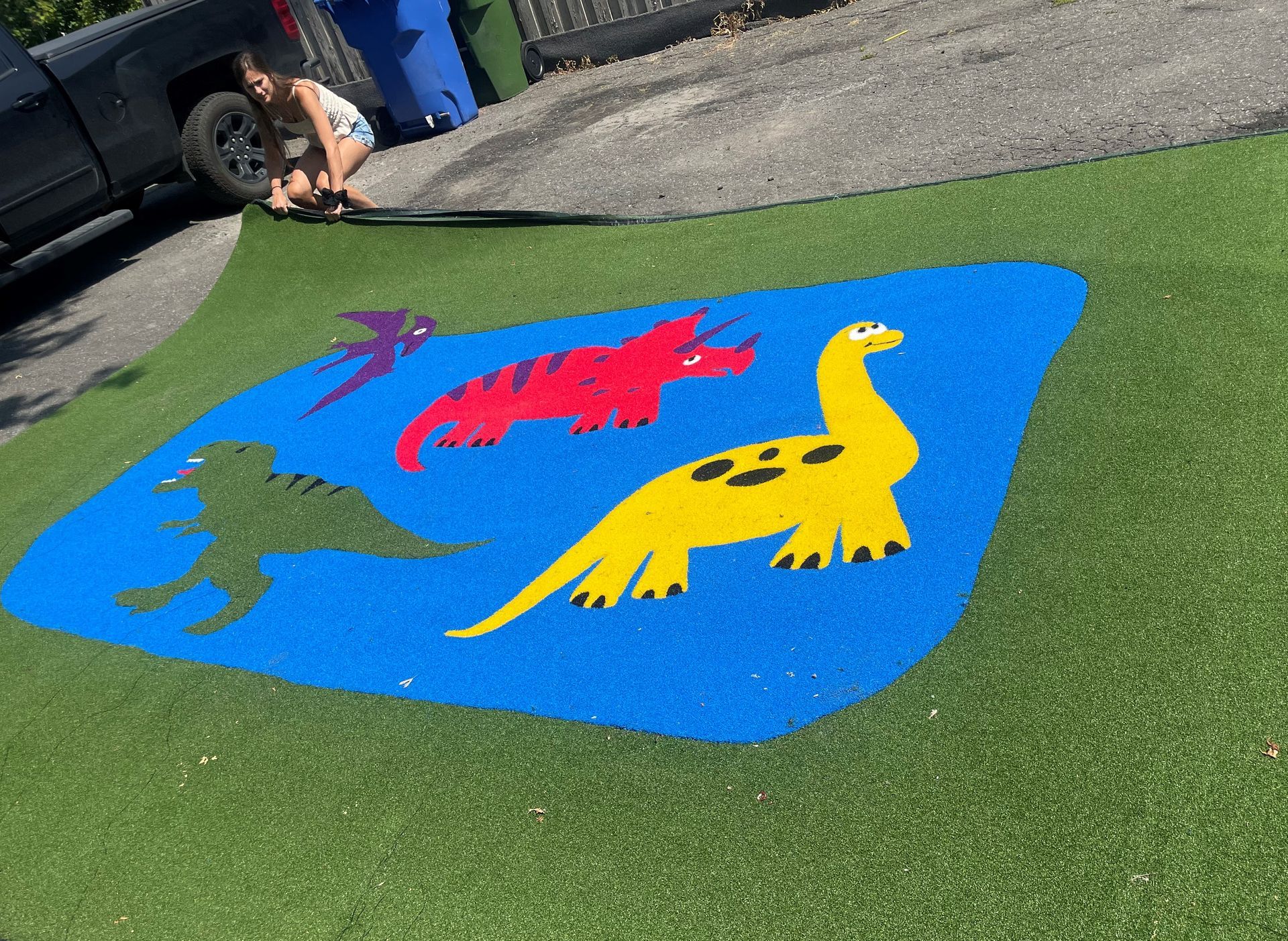 Aire de jeux avec des dinosaures bleus sur gazon vert. Une personne se trouve à proximité.