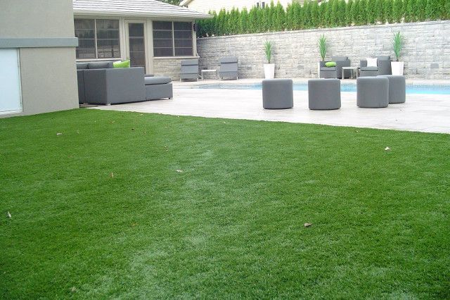 Gazon artificiel vert dans une cour arrière avec piscine, mobilier de patio et mur de pierre.