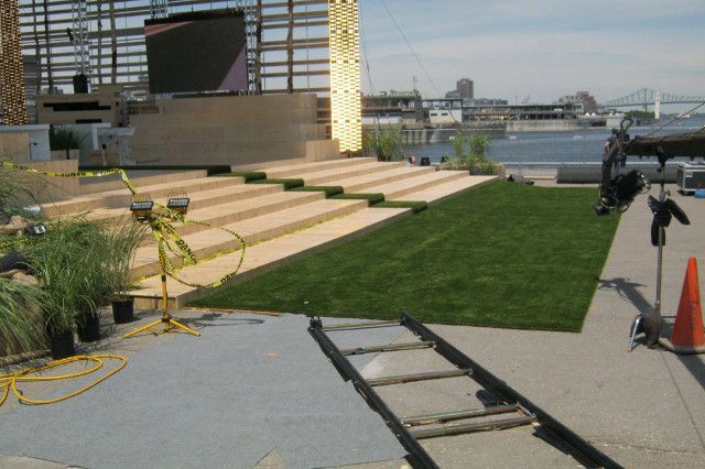 Scène sur le toit avec marches et pelouse ; piste de caméra au premier plan. Horizon urbain en arrière-plan.