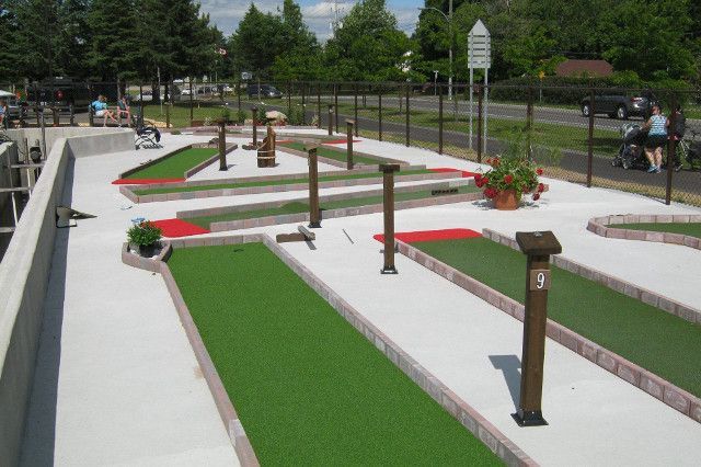 Mini-golf avec gazon artificiel vert, bordures en briques et poteaux en bois. Des joueurs jouent dans un parc.