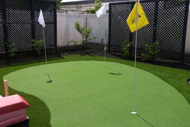 Un petit putting green dans l'arrière-cour avec trois trous et des drapeaux ; deux blancs et un jaune.