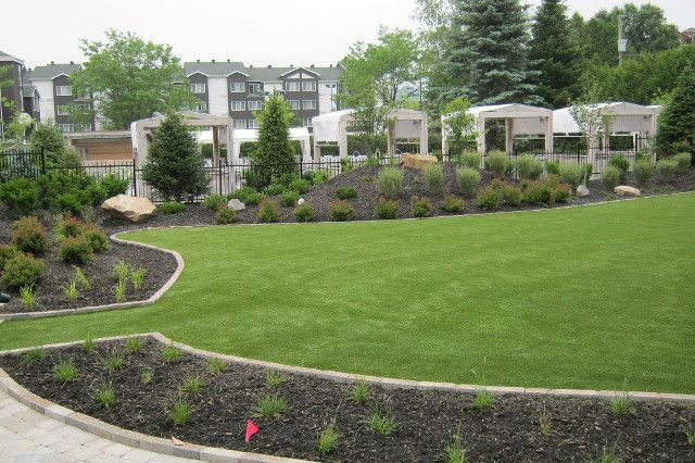 Pelouse verte luxuriante bordée de lits de paillis foncés et d'aménagement paysager avec de petites structures décoratives en arrière-plan.