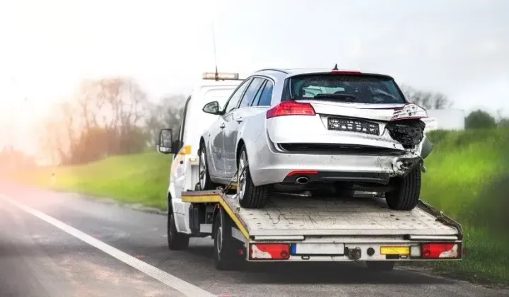 Silver car being loaded onto a flatbed tow truck on a roadside at dusk