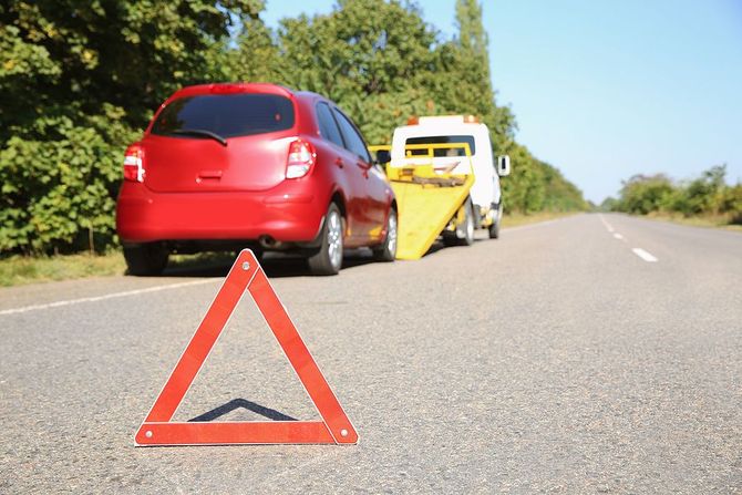 Red car with roadside warning triangle being towed on a highway shoulder