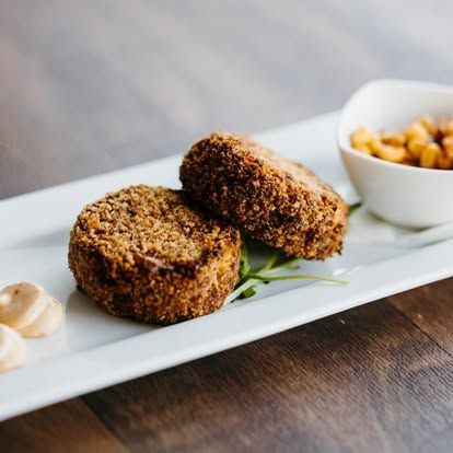 Two breaded croquettes on a white plate with dipping sauce on a wooden table