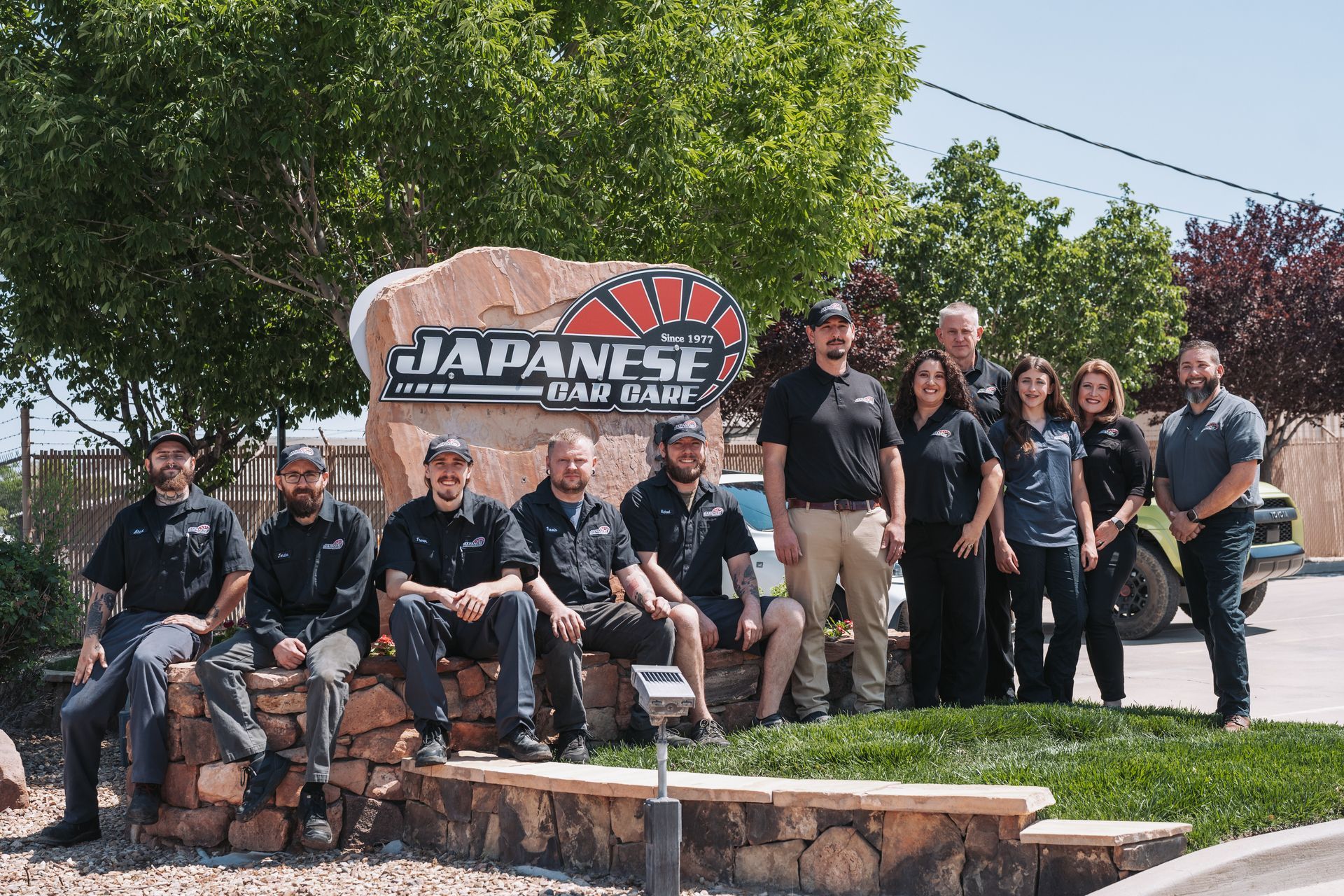 A group of people are posing for a picture in front of a large rock. | Japanese Car Care