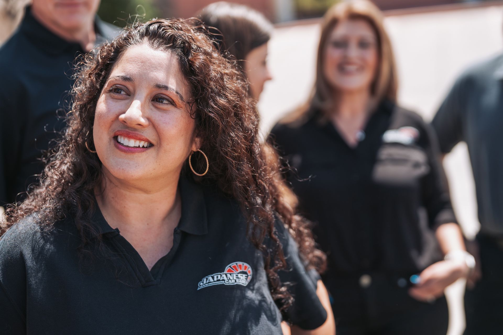 A woman in a black shirt is smiling in front of a group of people. | Japanese Car Care