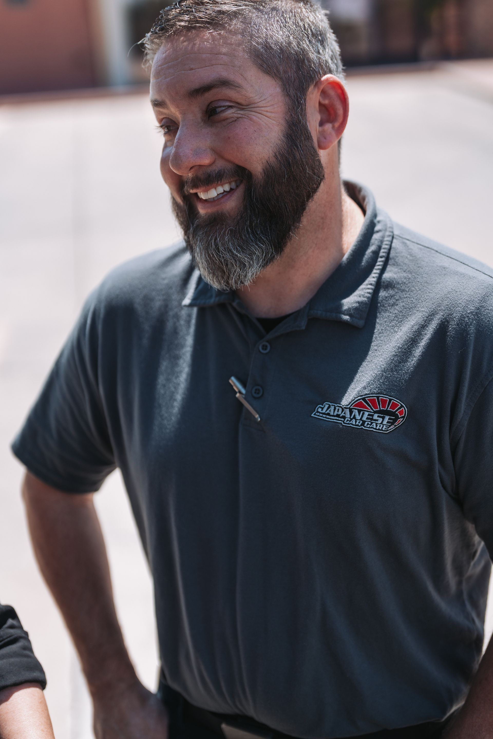 A man with a beard is wearing a polo shirt and smiling. | Japanese Car Care