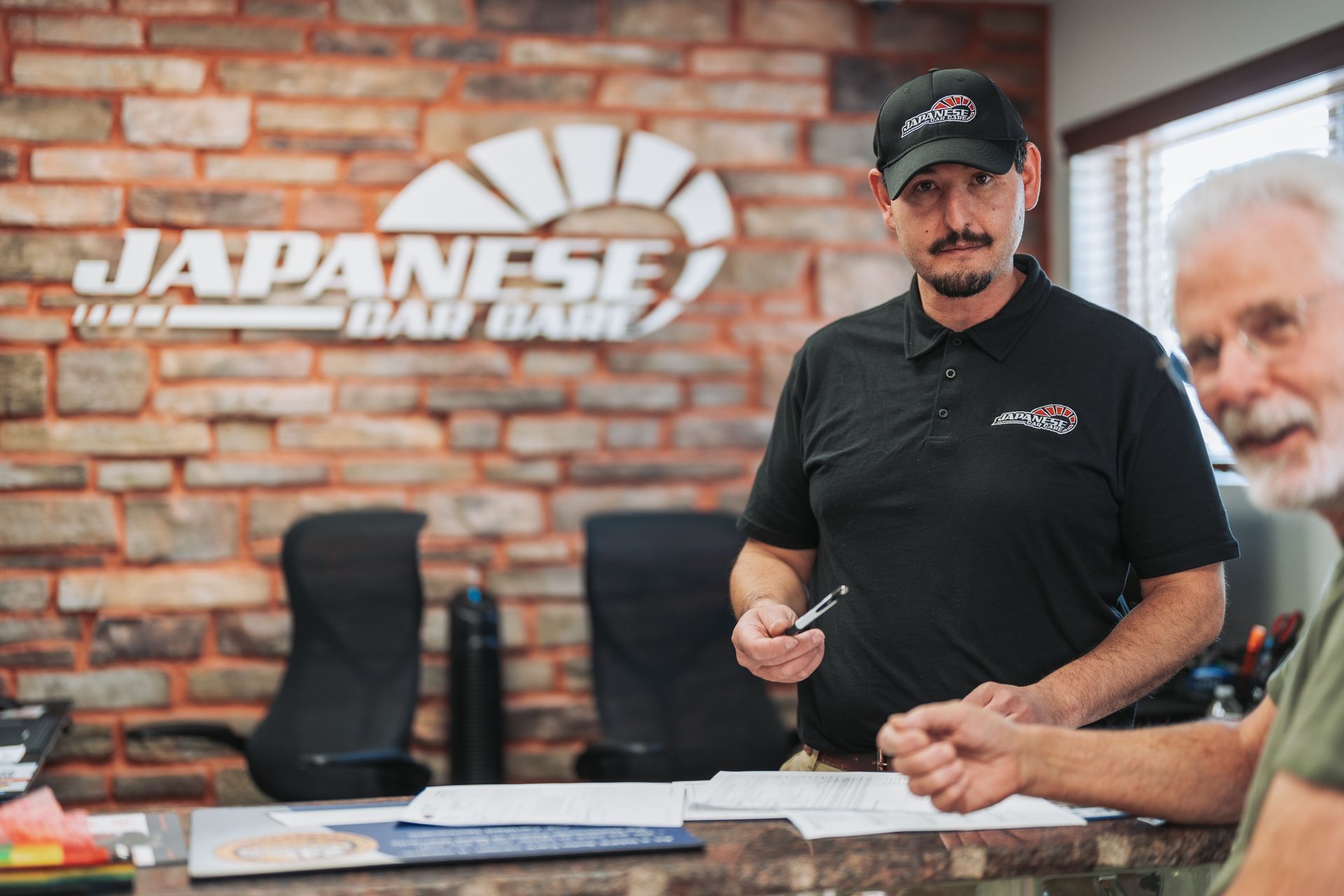 A man in a black shirt is standing in front of a japanese bank sign. | Japanese Car Care