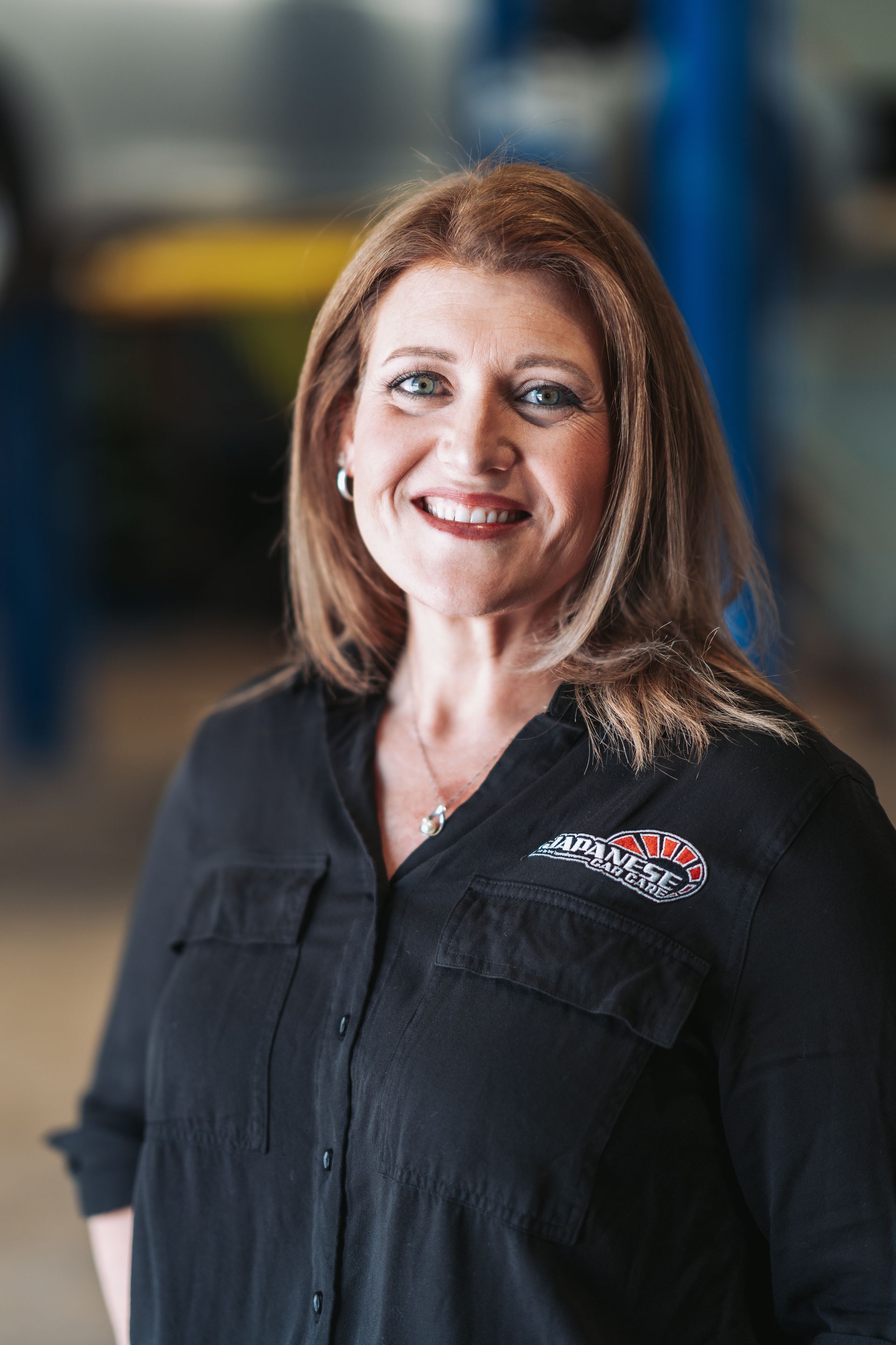 A woman in a black shirt is smiling in a garage. | Japanese Car Care