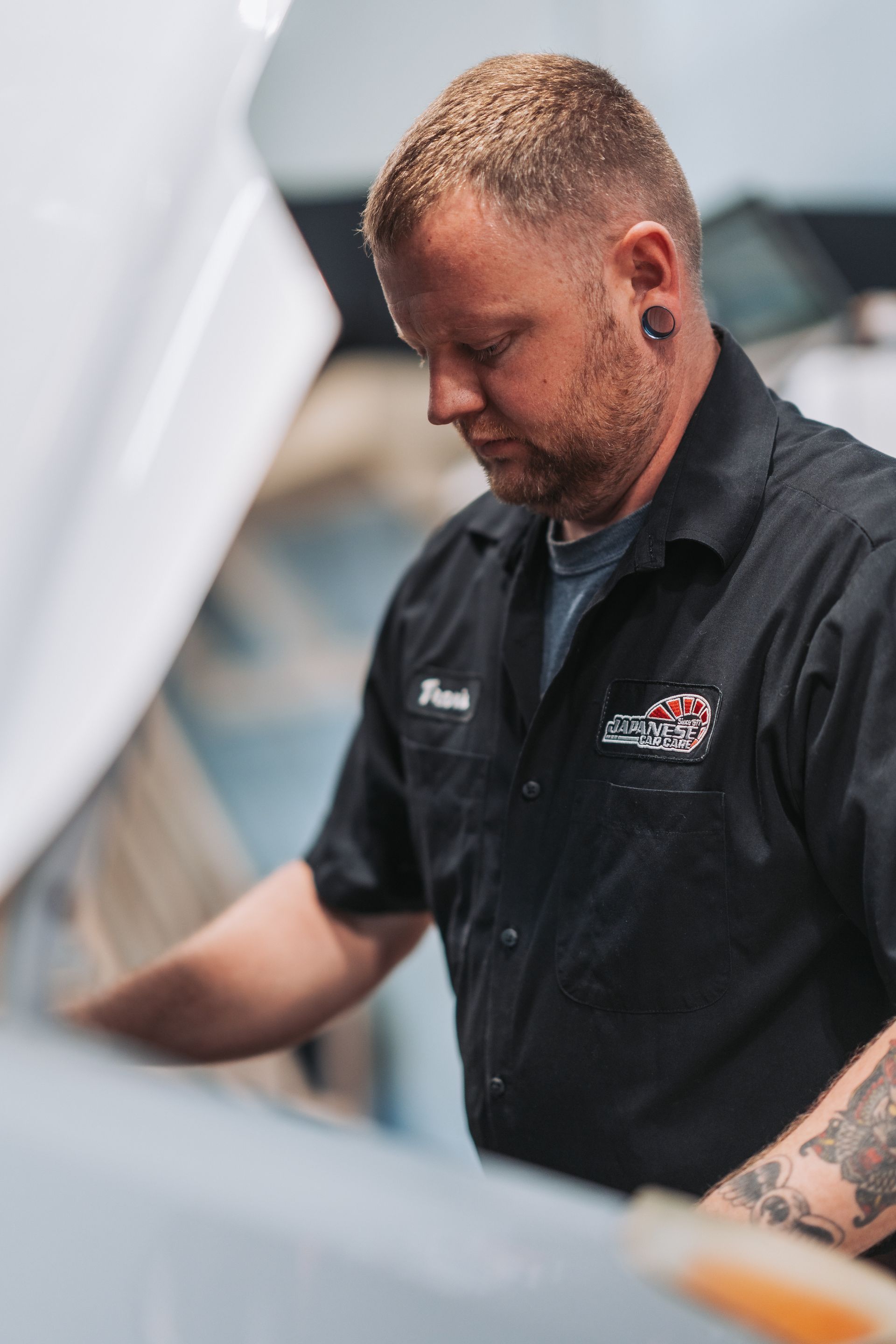 A man in a black shirt is looking under the hood of a car. | Japanese Car Care