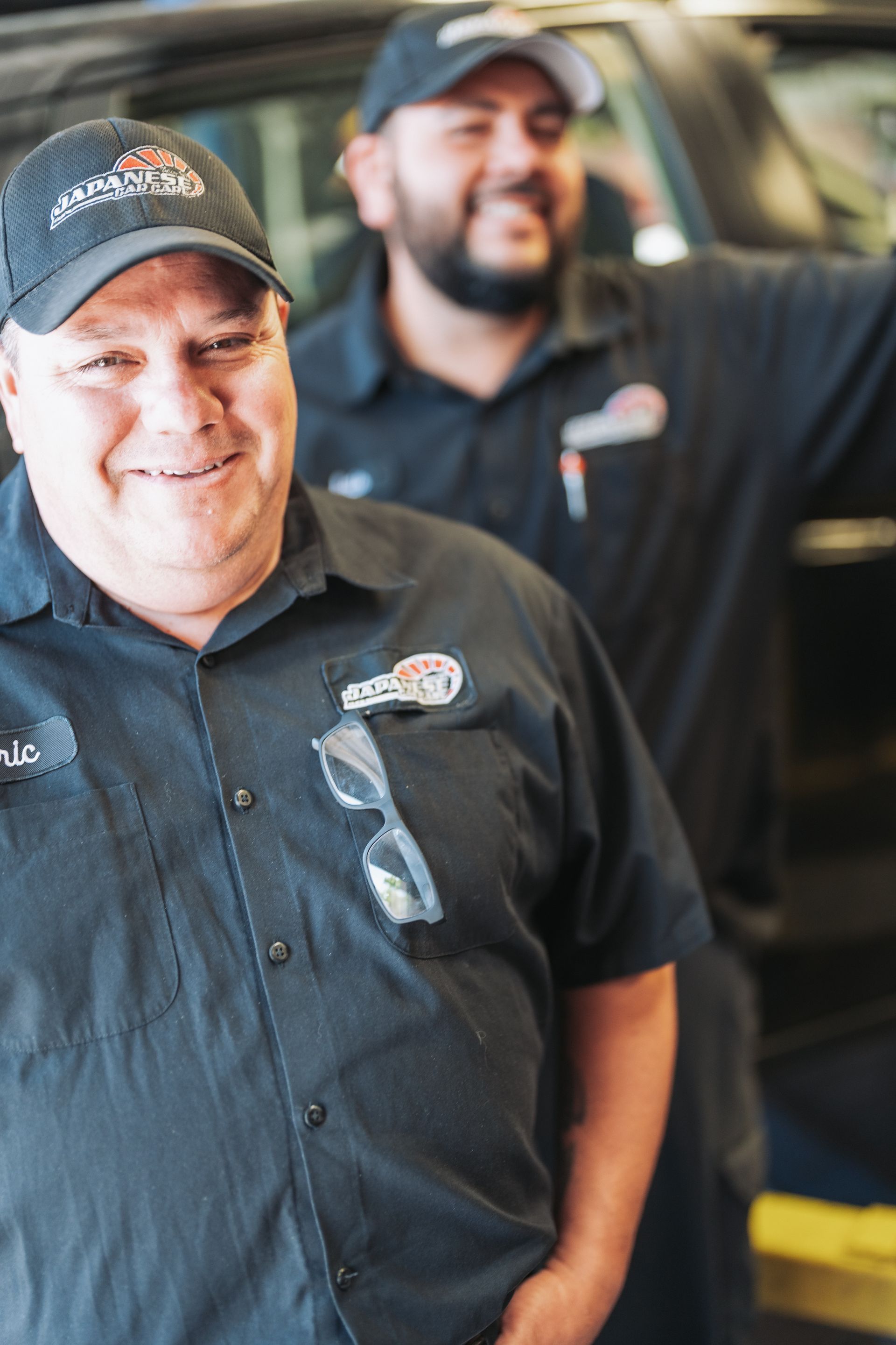 Two men are standing next to each other in front of a car in a garage. | Japanese Car Care