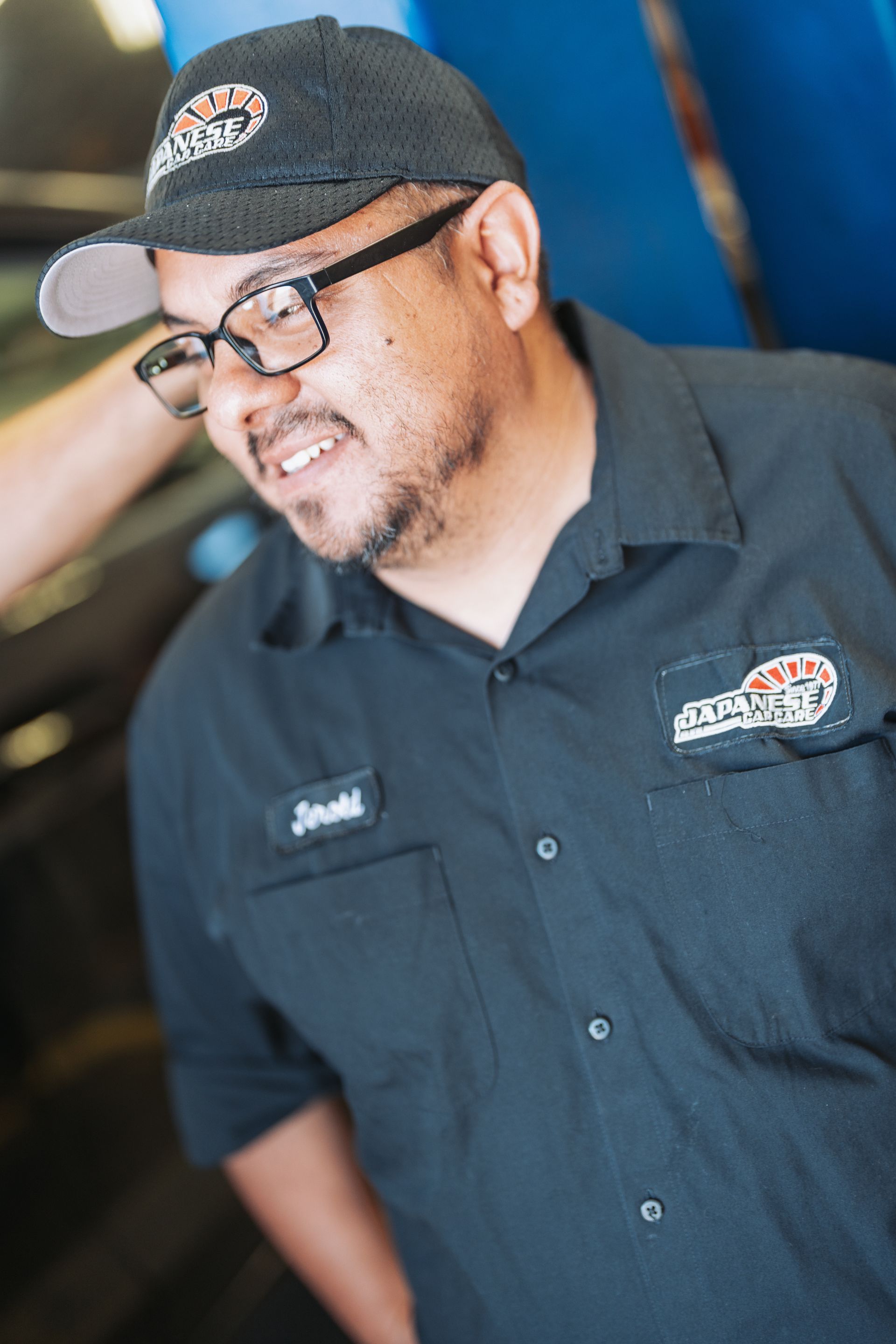 A man wearing a hat and glasses is standing in front of a car. | Japanese Car Care