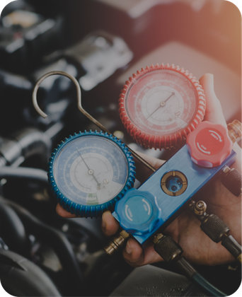 A person is holding two gauges in front of a car engine | Japanese Car Care