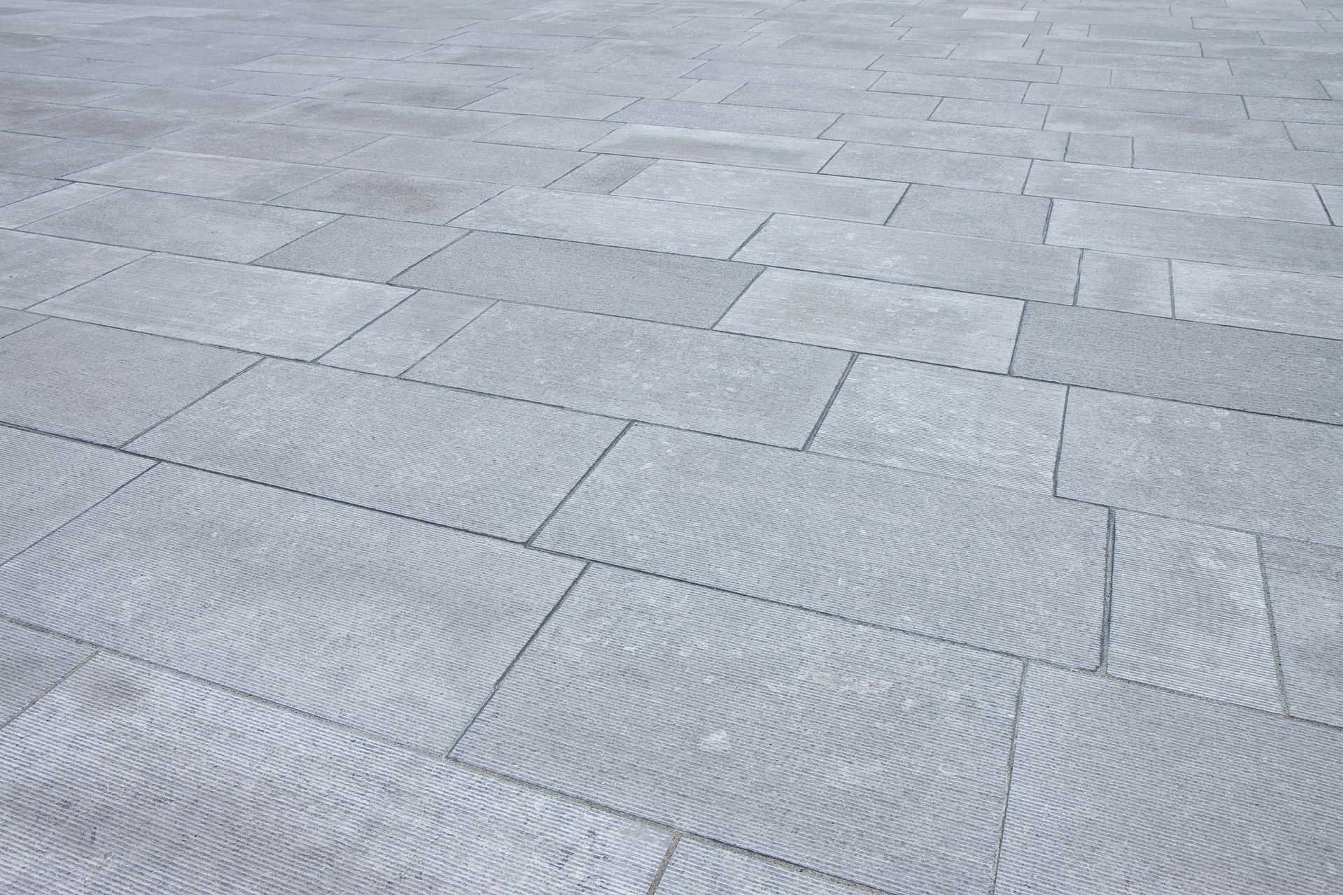 An angled, close-up view of a paved ground surface made of rectangular, textured grey stone tiles.
