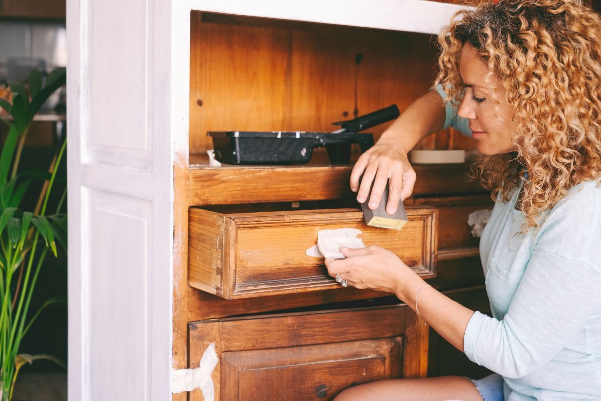Lady with curly hair upcycling her wooden cabinets by painting them.