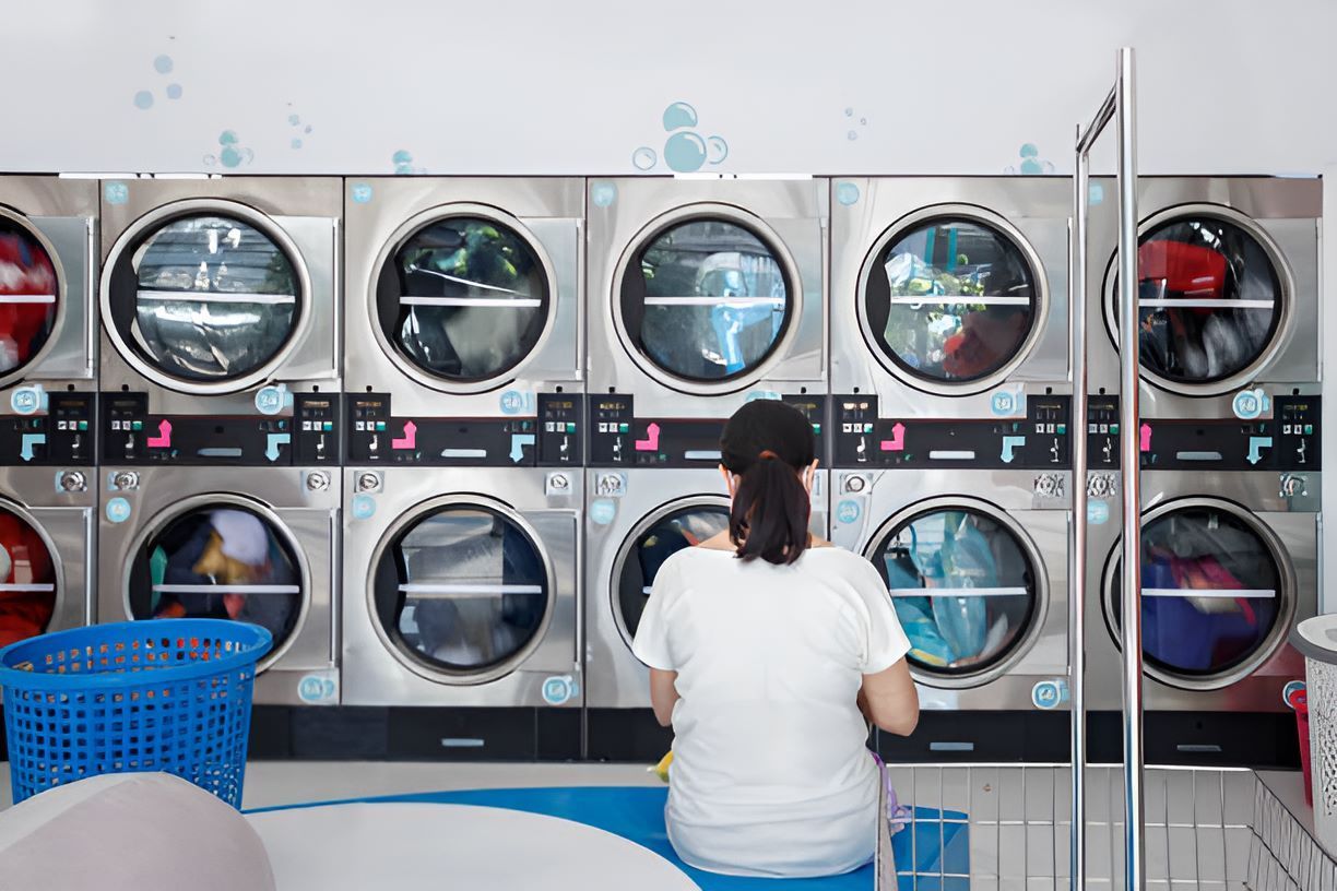 A Woman is Sitting in Front of a Row of Washing Machine — Super Suds Commercial Laundry in Avoca, QLD